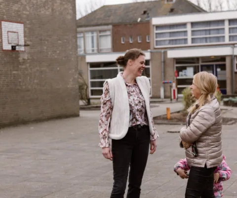 Leraar buiten in gesprek met ouder en kind