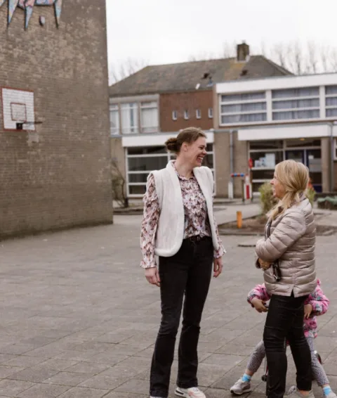 Leraar buiten in gesprek met ouder en kind